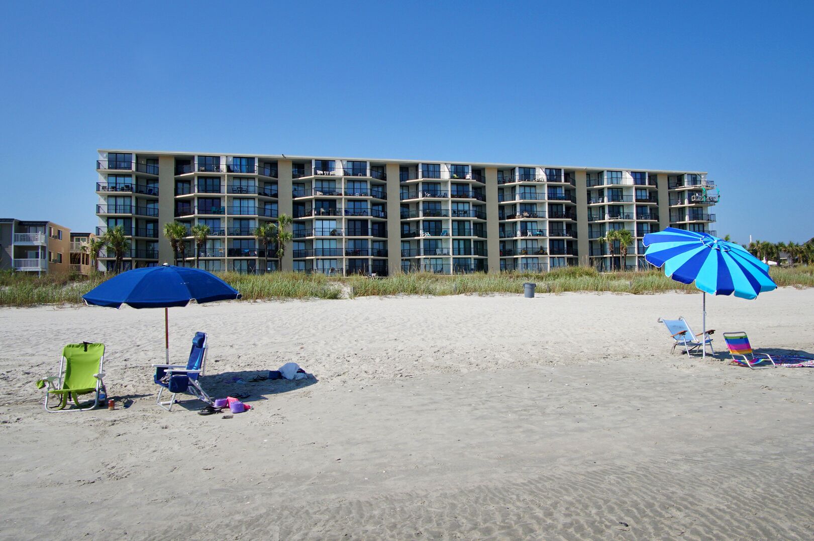 A beachfront hotel with multiple balconies and a sandy beach area with beach chairs and umbrellas.