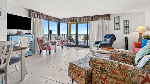 A spacious living room with a balcony, a television, and a dining area with a table and chairs. - Spacious, oceanfront family condo rental w/amazing views, pool, hot tubs in North Myrtle Beach (North Myrtle Beach)