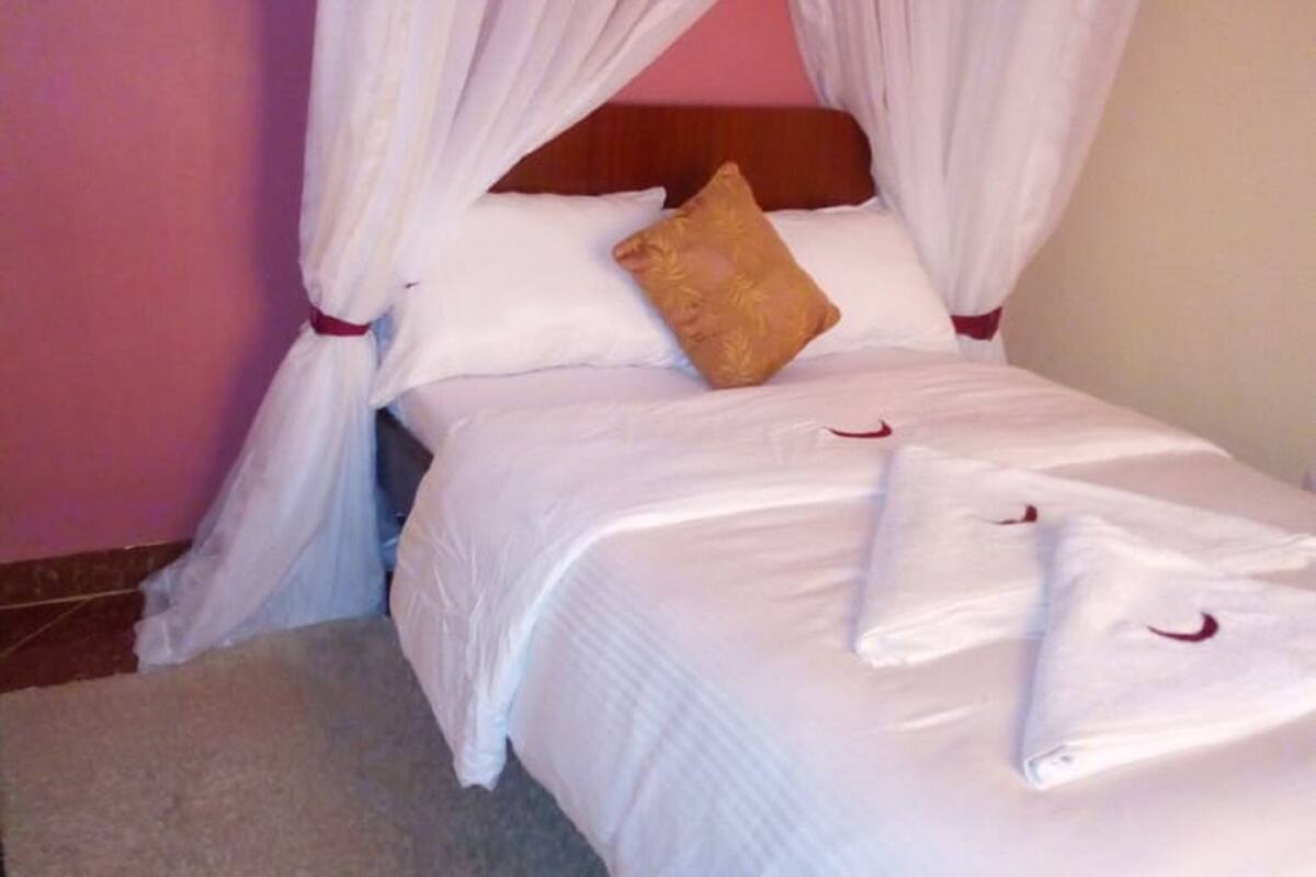 A bed with white bedding and a brown pillow, draped with white curtains.