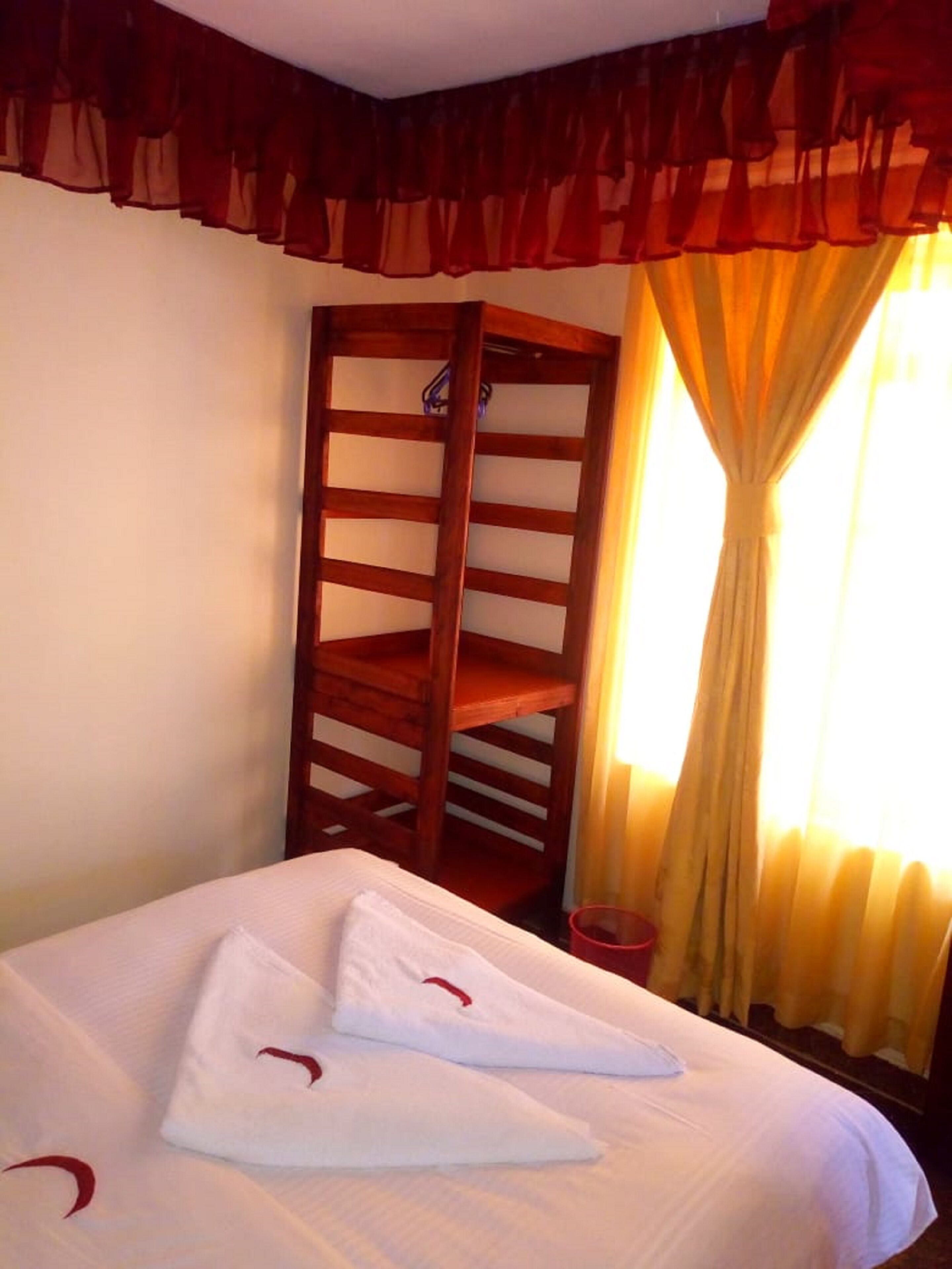Una habitación de hotel con cama, armario de madera y ventana con cortinas.
