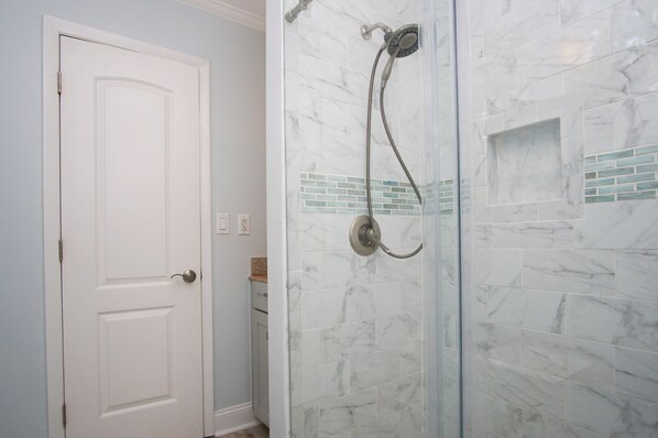 Un baño con mampara de vidrio, baldosas de mármol blanco y una puerta blanca.