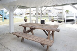 A wooden picnic table with benches under a covered area with white pillars.