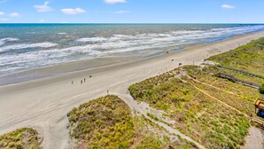 A beach with a clear view of the ocean, a sandy path, and a grassy area with a wooden walkway. - Premier resort offering deluxe oceanfront condos in the heart of family-friendly North Myrtle Beach (North Myrtle Beach)