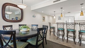 A dining area with a round table, chairs, and a mirror. There are hanging lights and a kitchen in the background. - Luxe oceanfront resort with pools, lazy river, hot tubs, spa, fitness center, poolside bar (North Myrtle Beach)