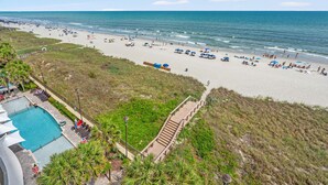 A beach with a swimming pool, beach umbrellas, and a wooden walkway leading to the beach. - Luxe oceanfront resort with pools, lazy river, hot tubs, spa, fitness center, poolside bar (North Myrtle Beach)