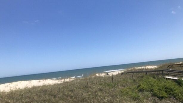 A beach with a wooden walkway leading to the water, sandy dunes, and sparse vegetation.