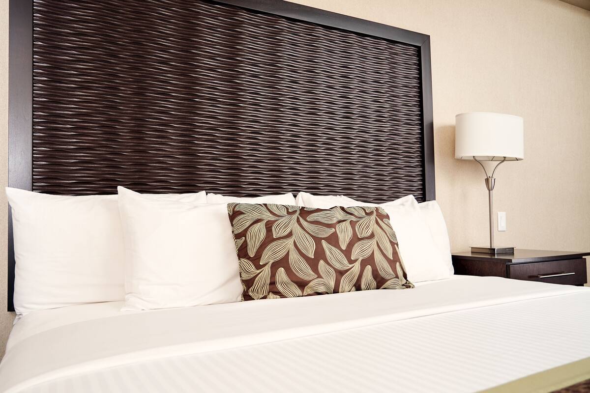 A hotel room with a bed, pillows, a lamp, and a nightstand.