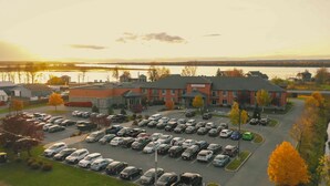 A parking lot with multiple cars, a building with a sign reading "Riverrock Inn", and a body of water in the background. - RiverRock Inn & Conference Centre (Clarence-Rockland)