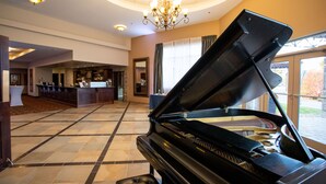 A grand piano in a spacious lobby with a chandelier, a bar area, and large windows. - RiverRock Inn & Conference Centre (Clarence-Rockland)