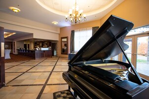 Um piano de cauda num amplo hall com um candelabro, zona de bar e grandes janelas.