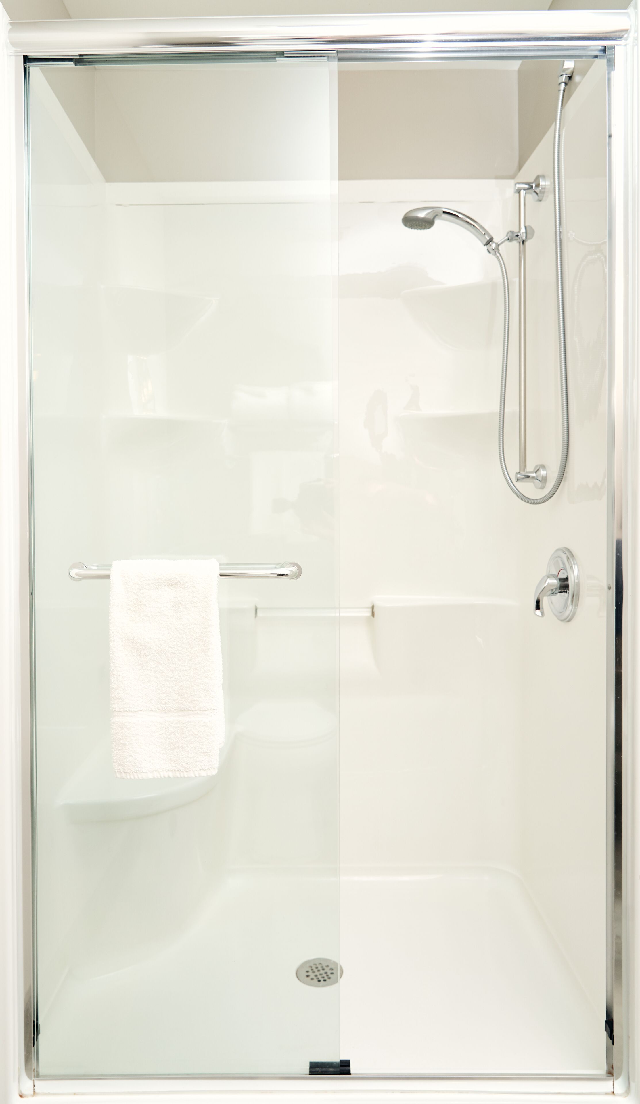 A glass-enclosed shower with a handheld showerhead and a handheld faucet.