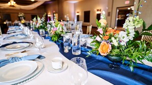 A banquet table set with white plates, blue napkins, and clear glassware, adorned with floral centerpieces. - RiverRock Inn & Conference Centre (Clarence-Rockland)