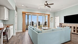 Ein geräumiges Wohnzimmer mit einem großen, hellblauen Sofa, einem Essbereich mit Küchenzeile und einem Balkon mit Sitzgelegenheit.