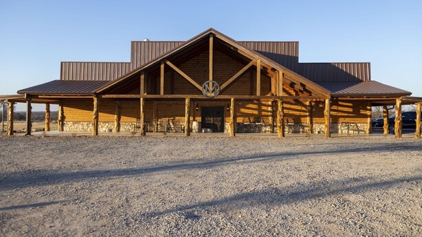 A large, rustic building with a prominent 'M' logo, featuring a covered patio area with seating and a stone wall. - Circle M Lodge is The Perfect Get-A-Way (Stratford)