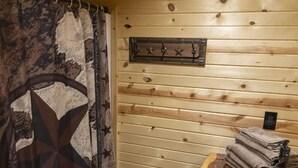 A wooden cabin interior with a rustic design, including a wooden wall, a star-patterned curtain, a metal sink, and a towel rack. - Circle M Lodge is The Perfect Get-A-Way (Stratford)