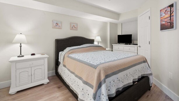 Une chambre à coucher comprenant un lit, des tables de chevet, un ventilateur de plafond, un téléviseur et un tableau accroché au mur.