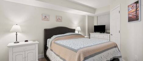 A bedroom with a bed, bedside tables, a ceiling fan, a television, and a painting on the wall.