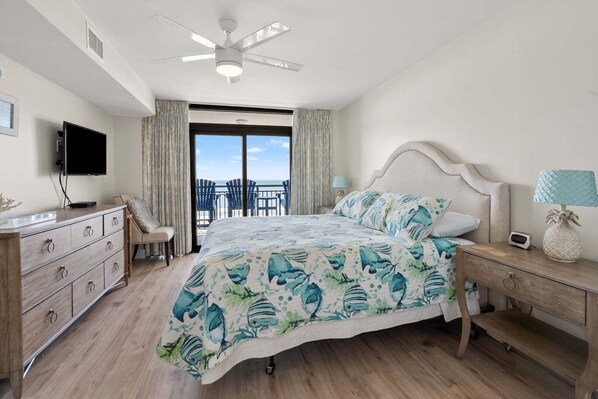 A bedroom with a bed, a TV, a desk, a chair, and a balcony with chairs.