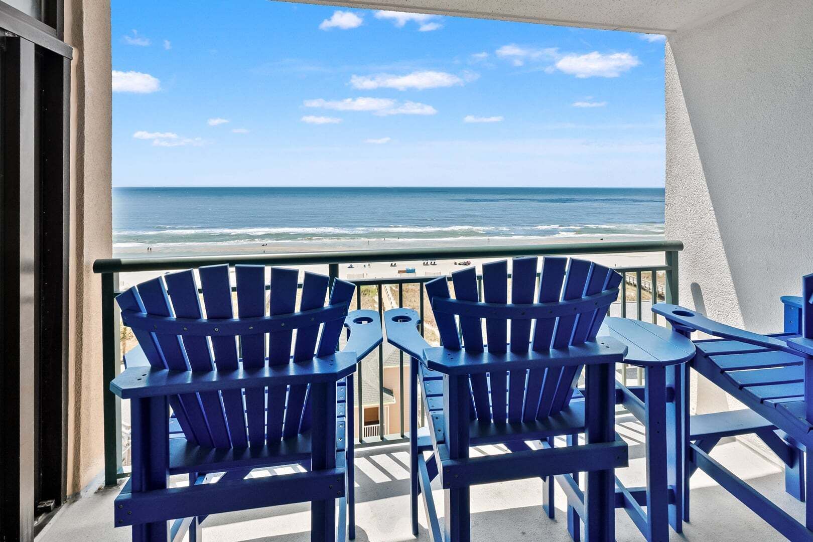 A balcony with two Adirondack chairs facing a beach.