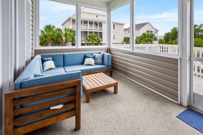 Relax in this serene sunroom with a view of palm trees and neighboring houses, featuring a comfortable sofa and wooden bench.