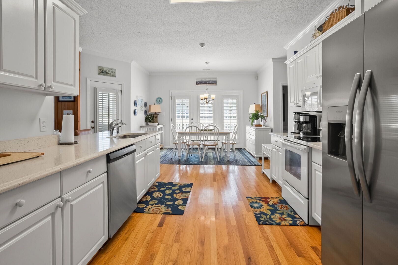 A kitchen with white cabinets, stainless steel appliances, a dining area with white chairs, and a wooden floor.