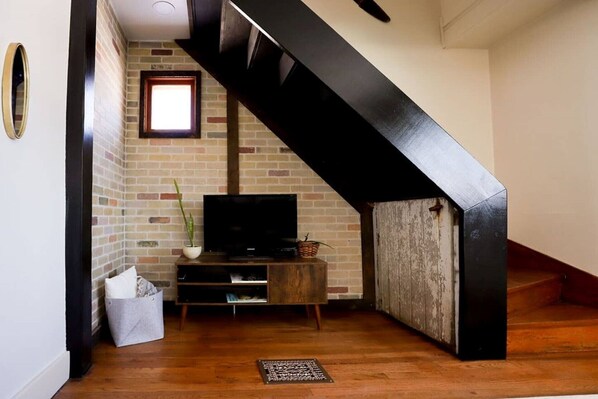 Stairs lead to an upper level, with a wooden entertainment unit featuring a flat-screen TV and a potted plant below.