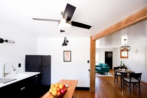 A modern kitchen with a black refrigerator, a wooden dining table with a bowl of fruit, and a ceiling fan.