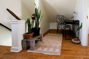 A serene retreat with a wooden floor, featuring a patterned rug, a small bench, and lush greenery.