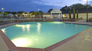 Une piscine avec une terrasse carrelée, des chaises longues et un kiosque.