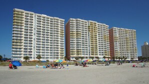 Un hotel frente a la playa con varios edificios altos, sombrillas y una playa de arena.