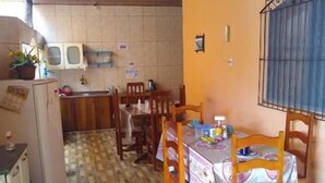 A compact kitchen with a tiled backsplash, wooden cabinets, and a dining area with a table and chairs. - Hotel Mapara Beach (Baiao)