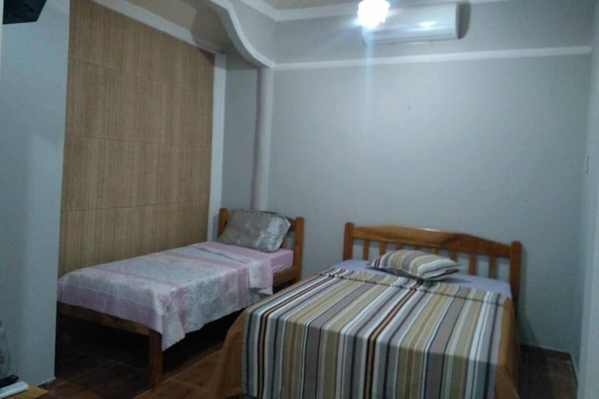 A small bedroom with two single beds, a wooden headboard, a wooden wardrobe, and a ceiling light.
