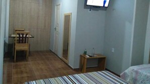 A small room with a bed, a television mounted on the wall, a wooden chair, and a small table with a bottle on it. - Hotel Mapara Beach (Baiao)
