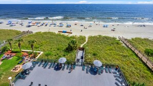 Ein Strand mit Sonnenschirmen und Liegestühlen, eine Holzterrasse mit Sitzgelegenheiten und Blick aufs Meer.