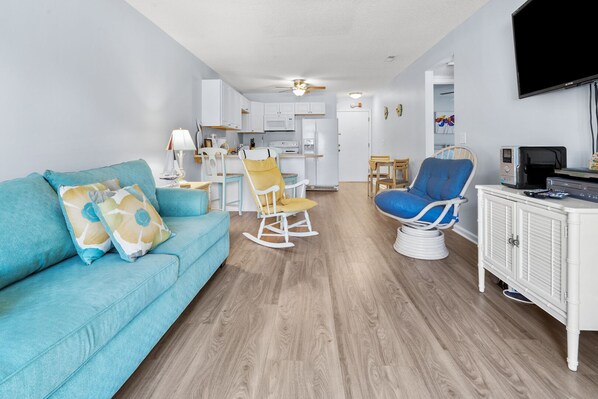 A modern living room with a blue sofa, a rocking chair, and a blue armchair. - Charming Condo Steps from the Beach with Pool, Sundeck, and Stunning Views in Vibrant Cherry Grove! (North Myrtle Beach)