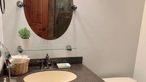 A bathroom with a round mirror, a sink, a toilet, and a small potted plant. - Beautiful center of Kalispell apartment (Kalispell)
