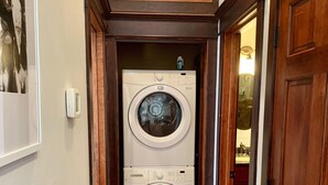 A laundry room with two stacked front-loading washing machines, wooden doors, and a hallway with wooden flooring. - Beautiful center of Kalispell apartment (Kalispell)