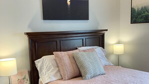 A neatly made bed with a pink quilt, a wooden headboard, and a nightstand with a lamp and a framed picture. - Beautiful center of Kalispell apartment (Kalispell)