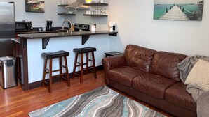A modern kitchen with a central island, bar stools, a brown leather sofa, and a painting of a pier. - Beautiful center of Kalispell apartment (Kalispell)