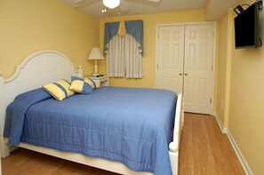A bedroom with a bed, a nightstand, a lamp, a window with curtains, and a door.