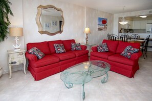 Un salon avec deux canapés rouges, une table basse en verre, une lampe blanche, un miroir décoratif et un tableau accroché au mur.