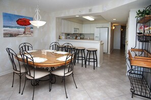 Un coin repas avec une table ronde, six chaises et une cuisine en arrière-plan.