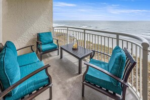 A balcony with a view of the ocean, furnished with two chairs and a table.