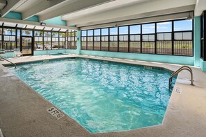 An indoor swimming pool with clear water, a tiled edge, and a safety railing.
