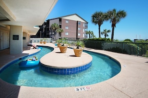 A swimming pool with a 3 FT depth marker, surrounded by potted plants and a building in the background. - Luxury oceanfront resort-workout room, indoor/outdoor pools, lazy river, kids' pool-in Ocean Drive (North Myrtle Beach)