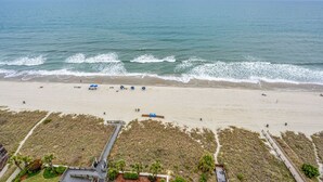 Una spiaggia con una passerella in legno che conduce a un edificio, una battigia sabbiosa e l'oceano.