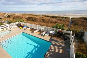 A pool area with a view of the beach, deck chairs, and a barbecue setup.