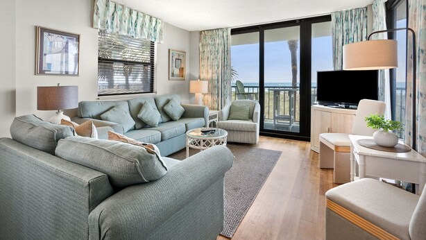 Un salon spacieux avec un canapé, des fauteuils, un téléviseur et un balcon offrant une vue agréable.