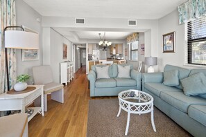 A modern living room with a sofa, a coffee table, and a dining area in the background.