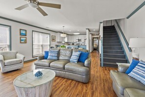 A spacious living room with a gray leather sofa, a glass coffee table, and a staircase leading to an upper level. - Gorgeous family ready oceanfront duplex, beautifully decorated, spacious oceanfront decks (North Myrtle Beach)